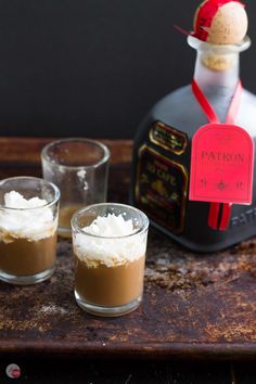 two shot glasses filled with chocolate pudding and whipped cream on a tray next to a bottle of patron