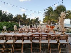 tables and chairs are set up on the beach for an outdoor wedding reception with palm trees in the background