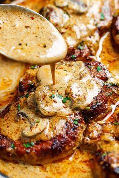 a wooden spoon is pouring sauce over some meats on a plate with potatoes and mushrooms