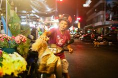 a man riding a motorcycle down a street next to flowers and other things on display