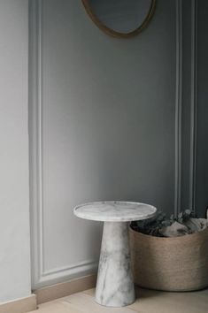 a white marble table sitting on top of a wooden floor next to a round mirror