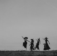 black and white photograph of four women in long dresses running across a field with kites flying overhead