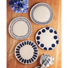 three plates with blue and white designs on them sitting on a wooden table next to flowers