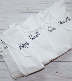 three personalized onesuits with names on them sitting on a white wooden surface