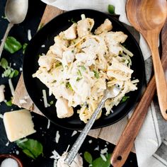 a black plate topped with pasta and cheese next to wooden spoons on a table