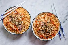 two bowls filled with noodles and carrots next to chopsticks on a marble surface