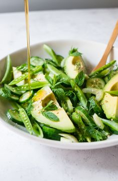 a white bowl filled with green vegetables and dressing being drizzled on top