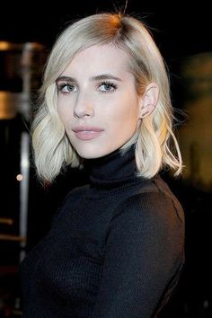 a woman with blonde hair wearing a black turtle neck sweater and jeans is looking at the camera