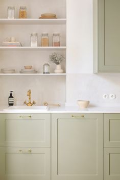 a kitchen with green cabinets and white counter tops, gold faucets and brass pulls