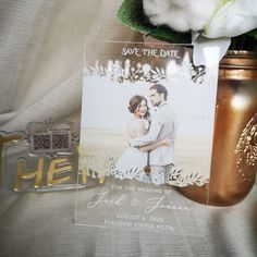 a gold vase with white flowers and a wedding photo on it next to a card that says save the date