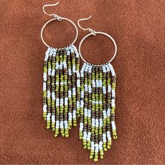 two green and white beaded earrings sitting on top of a brown carpeted floor