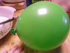 a green balloon sitting on top of a wooden table next to a bowl and knife