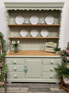 a green china cabinet with plates on top and flowers in vases next to it