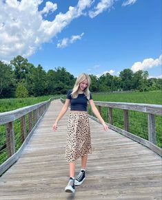 a woman walking across a wooden bridge