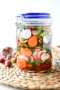 a glass jar filled with sliced carrots and radishes on top of a woven place mat