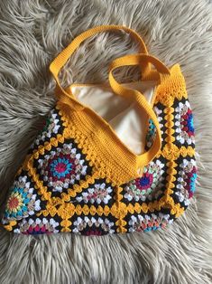 a crocheted purse sitting on top of a fluffy white rug with a yellow handle