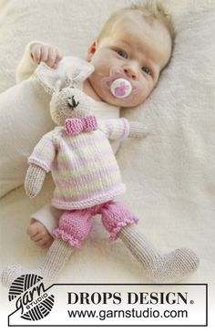 a baby laying on top of a white blanket next to a stuffed animal wearing a pacifier