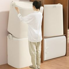 a woman standing next to two white refrigerators in a room with wood floors and walls