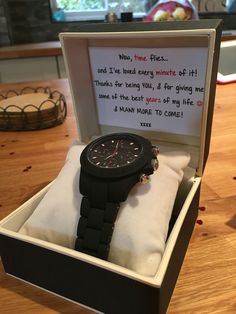 a watch sitting in a box on top of a wooden table next to a note