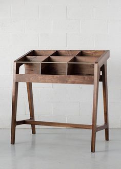 a wooden table with compartments on the top and bottom, against a white brick wall