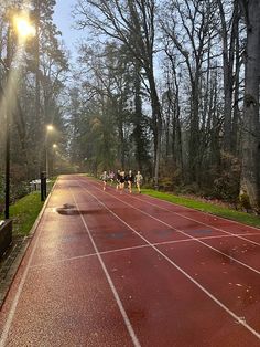 people are running on a red tennis court in the park at sunset or early morning