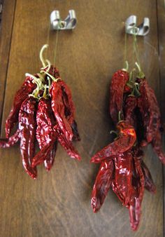 two red peppers hanging from hooks on a wooden table