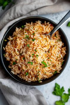 a black bowl filled with rice and garnished with parsley on the side