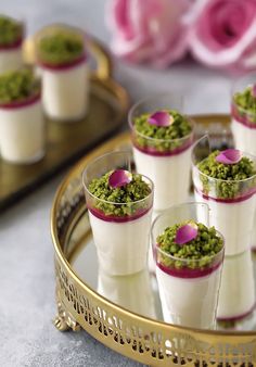 small cups filled with green and white desserts on a gold serving tray next to pink flowers