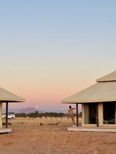 two large tents in the middle of an open field with people standing outside at sunset