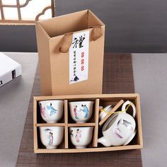 an open box with six cups and a teapot in it on top of a table