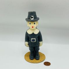 a small toy figurine with a hat on it's head standing next to a penny