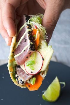 a person is holding a sandwich with meat and veggies on it next to a slice of lime