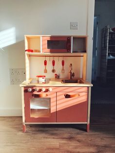 a wooden play kitchen with red appliances and cupboards