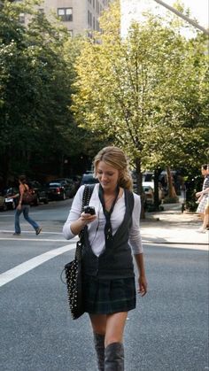 a woman is walking down the street while looking at her cell phone and holding a purse