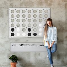 a woman sitting on a bench in front of a wall with holes and circles painted on it