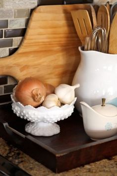 an assortment of kitchen utensils and garlic on a wooden tray in front of a brick wall