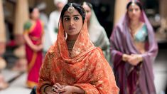 a woman dressed in an orange sari standing next to other women wearing colorful clothing