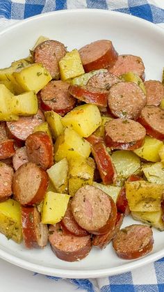 a white plate topped with sausage, potatoes and tomatoes on top of a blue and white checkered table cloth