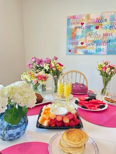 a table topped with plates of food next to vases filled with flowers and fruit