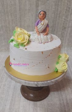 a white cake with yellow flowers and a woman sitting on top of the frosted cake