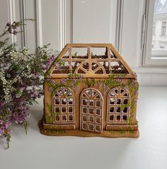 a house shaped planter sitting next to a vase with purple flowers in front of it