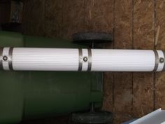 a white pipe is attached to the side of a green tank in a storage area