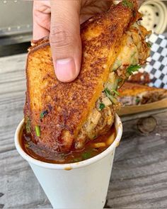 a person is holding up a grilled sandwich in a cup