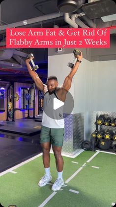 a man holding two dumbs while standing on top of a green mat in a gym