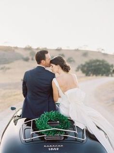 a bride and groom are riding on the back of a vintage car