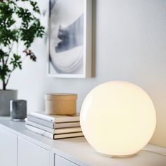 a white lamp sitting on top of a table next to some books and a potted plant