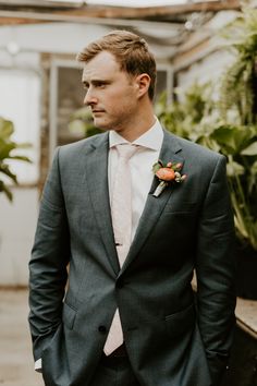 a man in a suit and flower boutonniere standing next to potted plants