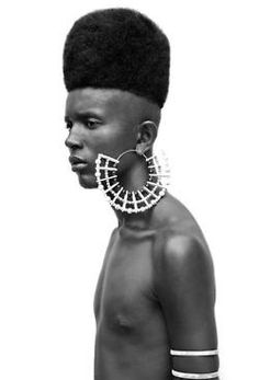 an african man with large hoop earrings on his face and neck, standing in front of a white background