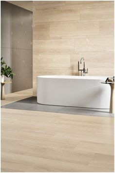 a white bath tub sitting on top of a wooden floor next to a planter