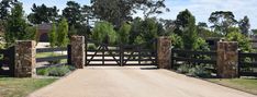 a gated driveway leading to a grassy area with trees in the background and bushes on either side